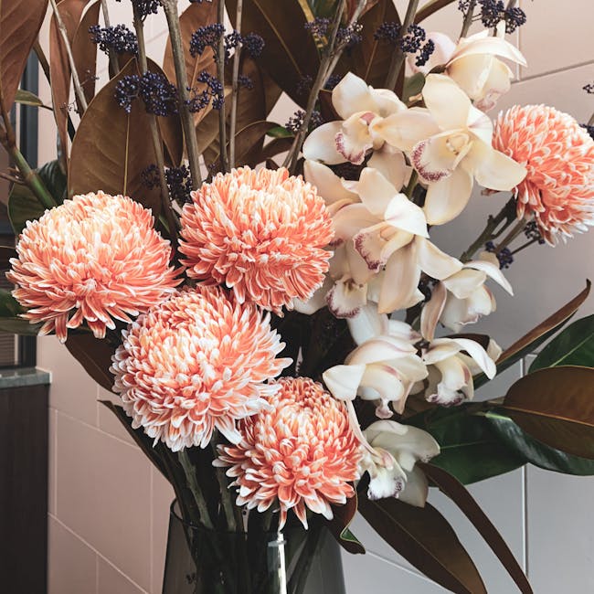 A vibrant floral arrangement featuring large, peach-pink chrysanthemum blooms with numerous densely packed petals, paired with elegant white orchids that have soft, rounded petals with subtle pink mar