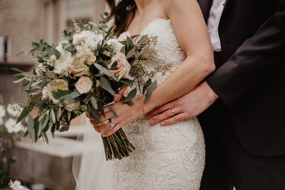 A close-up view of a bride and groom during a wedding ceremony, where the bride is holding a large bouquet of fresh flowers, featuring soft pink roses, white blooms, and green foliage including eucaly